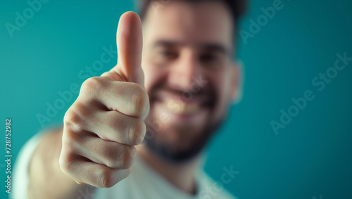 A man likes a turquoise background. Smiling handsome young man giving thumbs up and looking at camera.