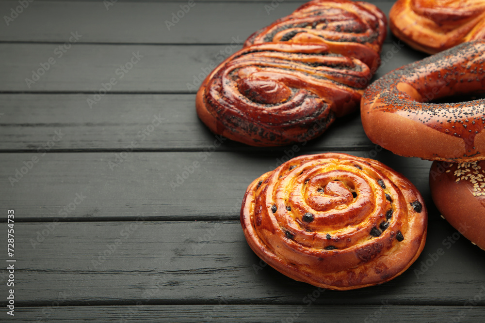 Fototapeta premium Bakery - various kinds of breadstuff. Bread rolls, bagel, sweet bun on black wooden background. Space for text