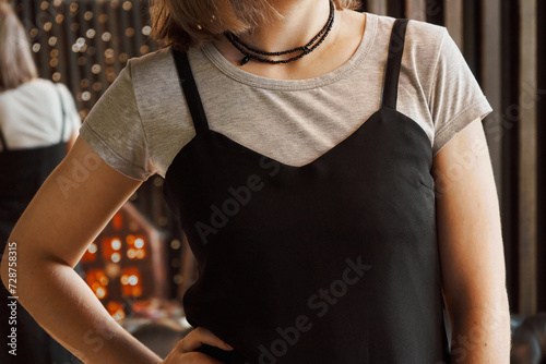 Woman wearing a black thin straps dress over a gray T-shirt. Concept: Combination of clothes from the wardrobe with each other and accessory jewelry. Black beaded beads in two rows hang on the neck