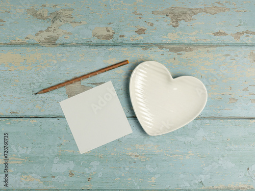 Heart shaped plate, paper, pencil on vintage wooden background. Top view.