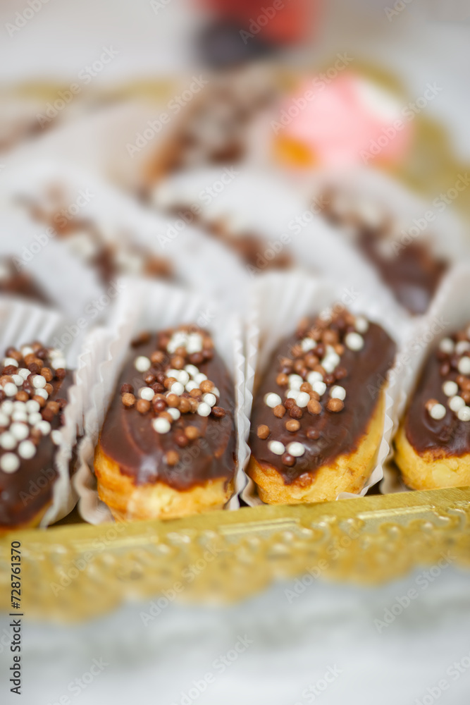 Small eclairs sweets backed pastry with colorful sprinkles close up