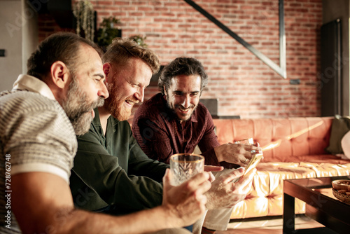 Group of men laughing and having drinks in a modern living room photo