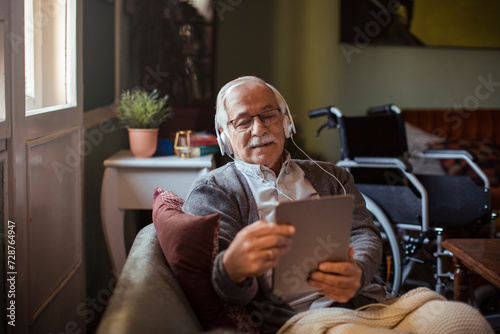 Senior man with headphones using tablet on home sofa photo