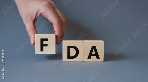 FDA - Food Drug Administration symbol. Wooden cubes with word FDA. Doctor hand. Beautiful grey background. Medical and Food Drug Administration concept. Copy space.