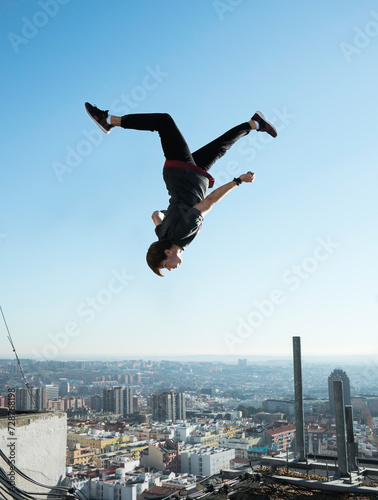 young boy doing parkour a backflip over blue sky on rooftop