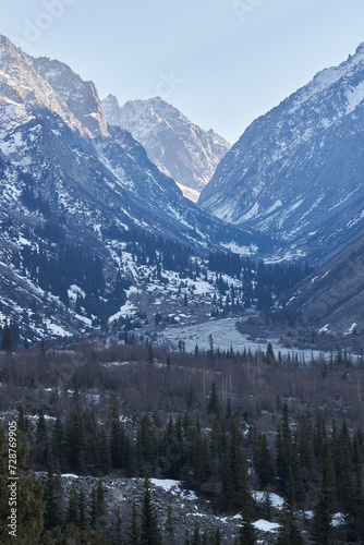 High rocky mountains with snow, illuminated by the warm setting sun. Natural landscape in Ala-Archa National Park. Spring in Kyrgyzstan. Coniferous forest in the shade. 