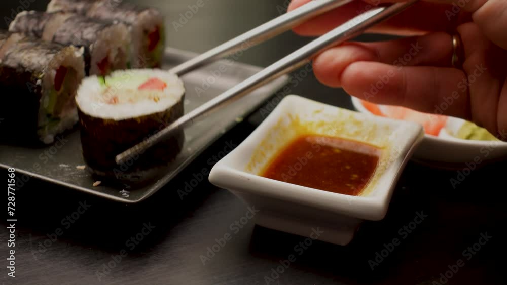Close up of hands with chopsticks eating japanese food. Traditional asian rolls. Maki sushi with vegetables and tuna Close up of hands with chopsticks eating japanese food. Traditional asian rolls. Maki sushi with vegetables and tuna