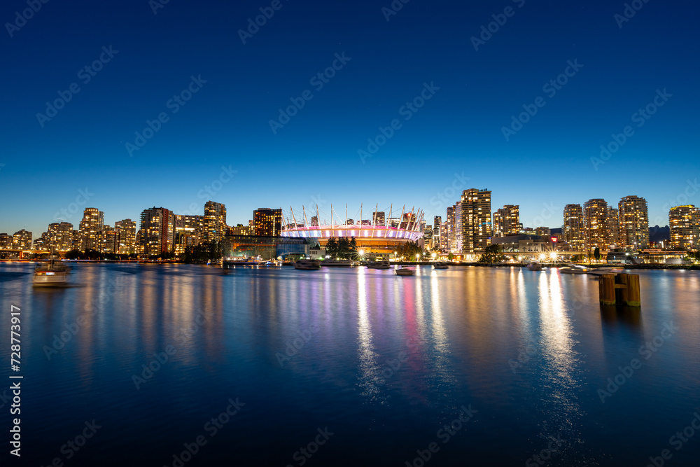 A long exposure photo during blue hour of the Vancouver Skyline from False Creek with the BC Place Stadium illuminated.