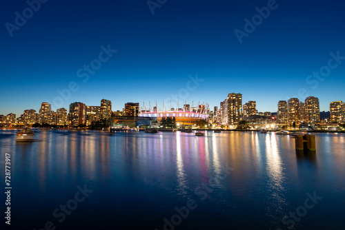 A long exposure photo during blue hour of the Vancouver Skyline from False Creek with the BC Place Stadium illuminated.