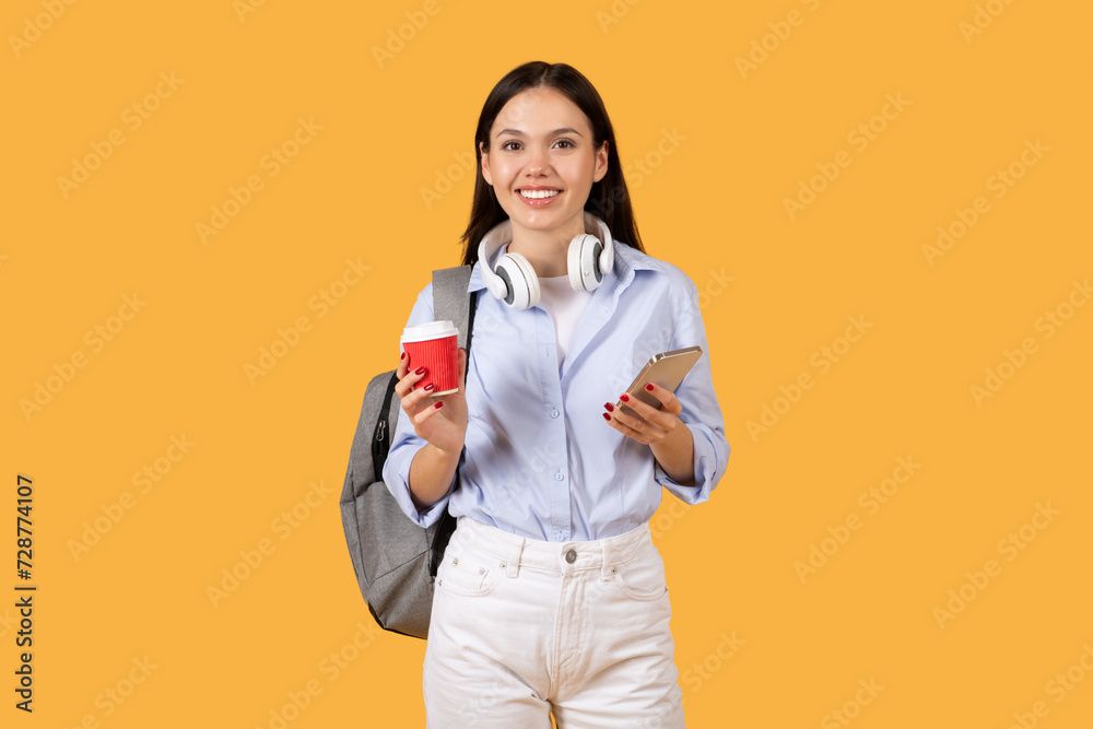 Lady student with coffee and phone, headphones on neck Lady student with coffee and phone, headphones on neck