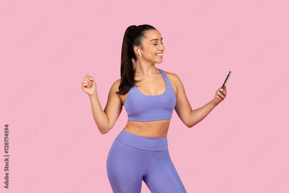 Joyful woman dancing with phone in lavender gym wear