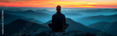 Man meditating on top of a mountain at sunrise, panoramic view