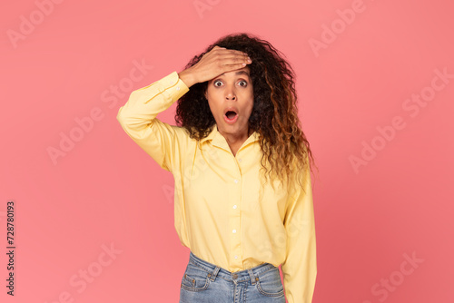 Shocked black woman with hand on forehead, wide-eyed, on pink background