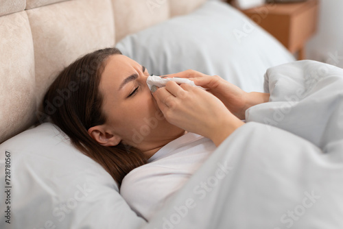 Young woman with cold, blowing her nose, lying in bed photo