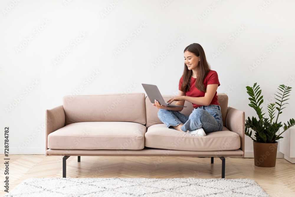 Relaxed young asian woman smiling while working on her laptop at home Relaxed young asian woman smiling while working on her laptop at home