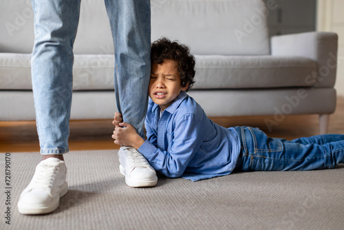 Upset child boy clinging to father's leg at home photo
