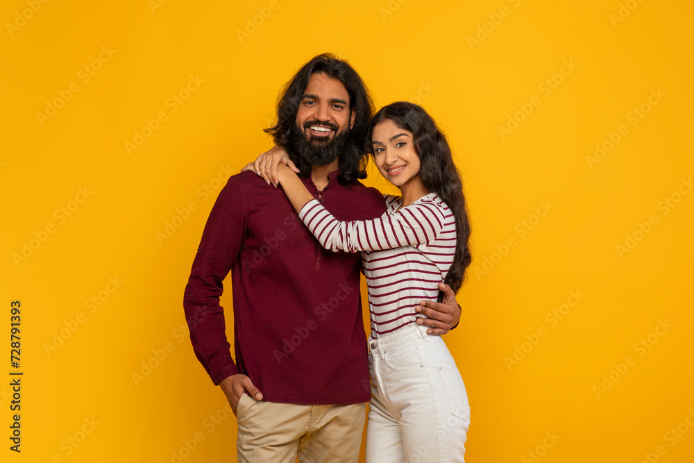 Happy young indian man and woman embracing on yellow background Happy young indian man and woman embracing on yellow background