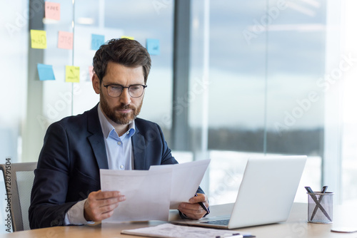 Cuadro en lienzo Serious thinking businessman behind paper work, mature experienced boss working with reports and financial documents, financier inside office with laptop, reading contract, thoughtfully checking