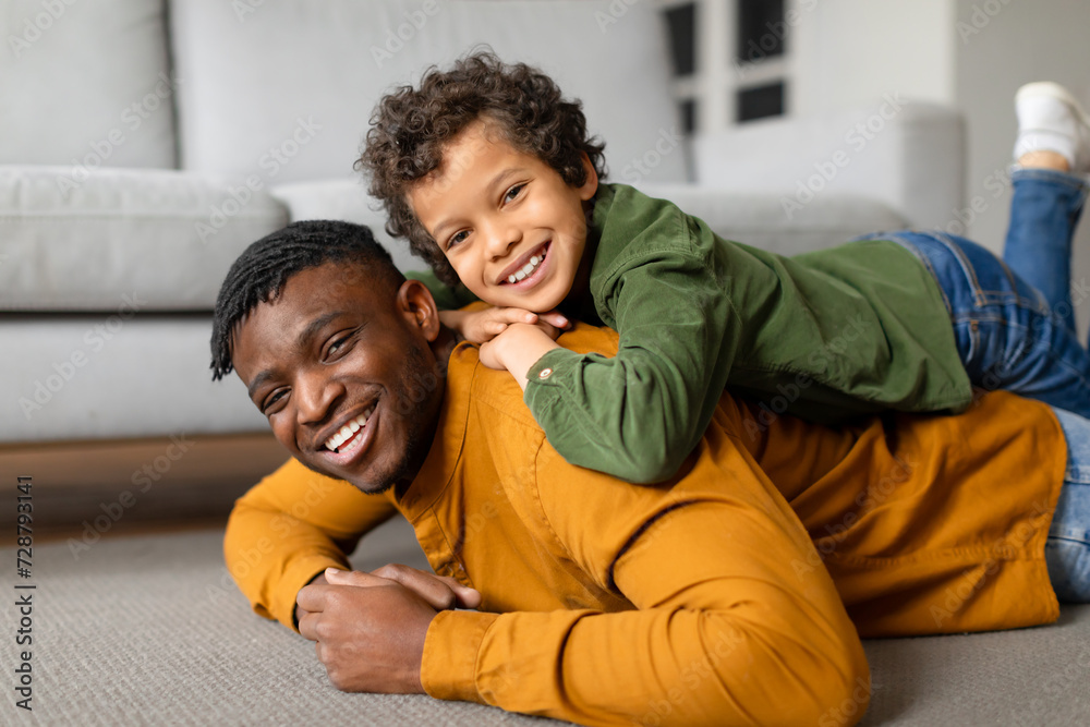 Black father and son share playful moment on the floor Black father and son share playful moment on the floor