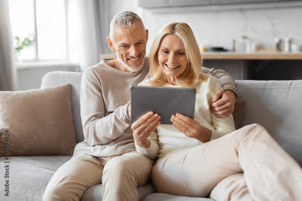 Positive retired couple using digital tablet at home Positive retired couple using digital tablet at home