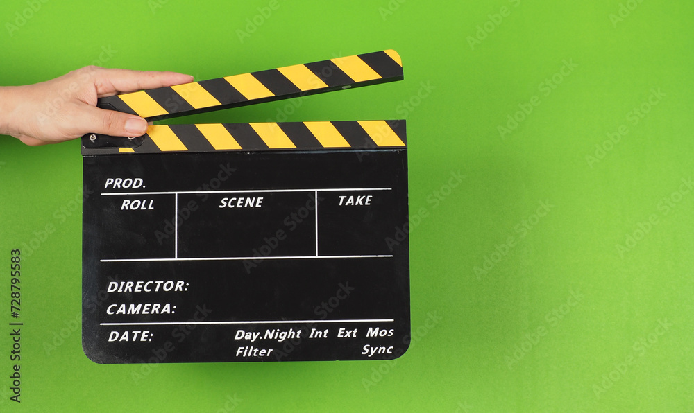 A yellow clapper board in hand on the green screen background.