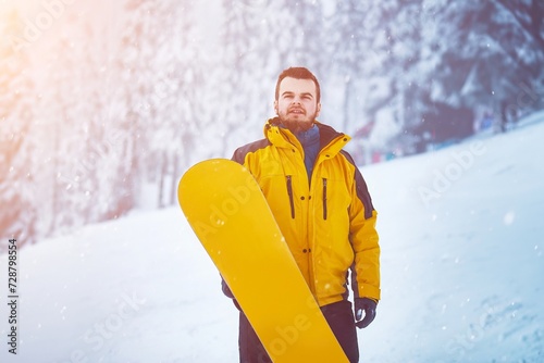 Man At Ski Resort with a snowboard On The snowy Background. Bearded man in winter landscape. Winter holidays in the snowy mountains with active sports.