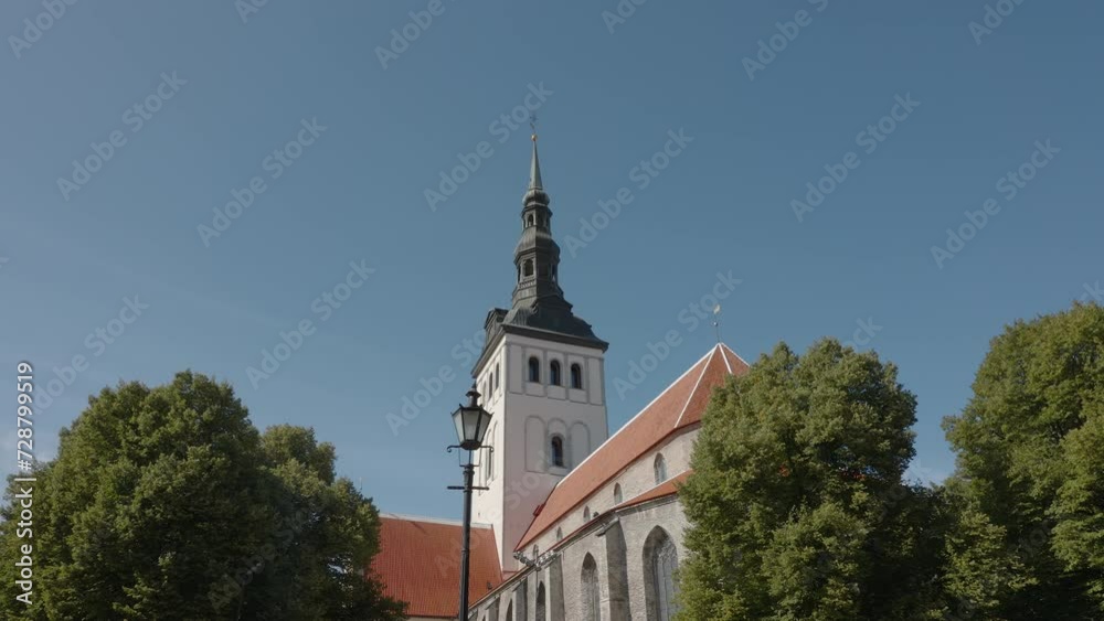 A serene view capturing the elegance of a historic church with its towering spire rising above lush green treetops under a clear blue sky in Tallinn on Estonia A serene view capturing the elegance of a historic church with its towering spire rising above lush green treetops under a clear blue sky in Tallinn on Estonia
