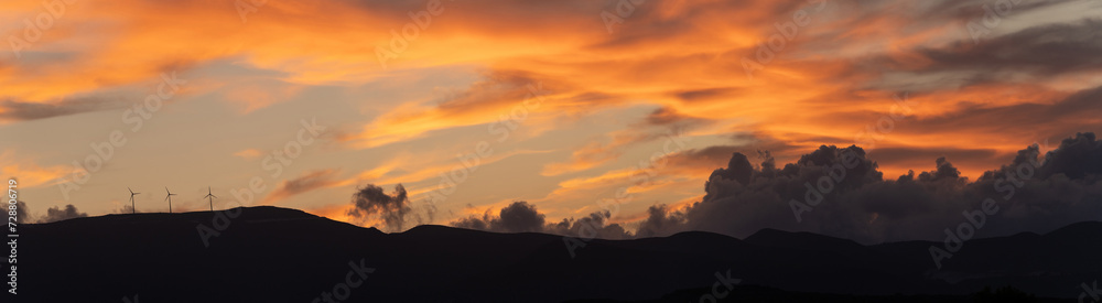Panorama shot of clean energy power concept with wind turbine on top of a mountain during dramatic sunset in zakynthos, Greece