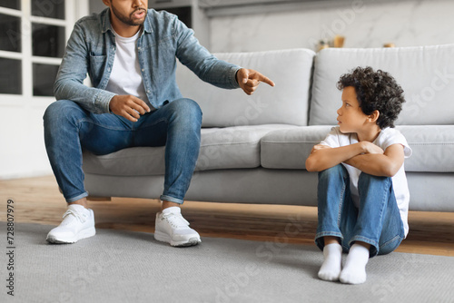 Young black father scolding his preteen son at home, pointing finger photo