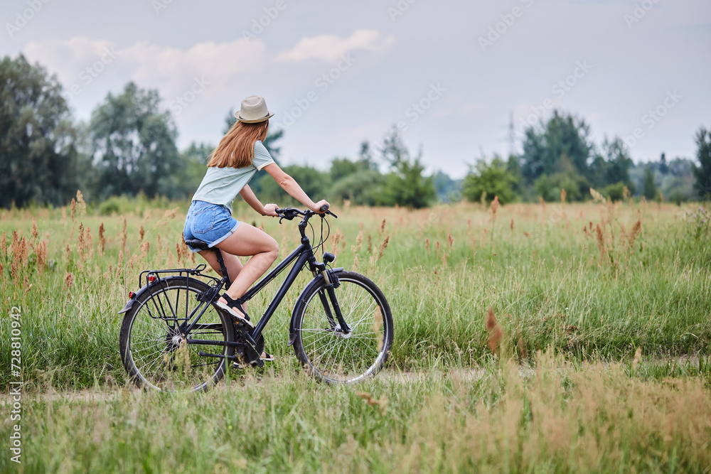 Woman riding bicycle on field or park in summer. Happy lady on bike having fun on coutry road. Summertime freedom and healthy lifestyle concept. Woman riding bicycle on field or park in summer. Happy lady on bike having fun on coutry road. Summertime freedom and healthy lifestyle concept.