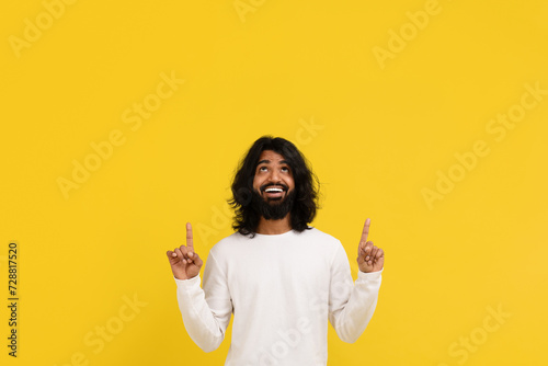 Amazed excited millennial indian guy pointing up at copy space