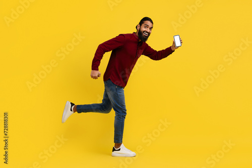 Bearded indian man running with smartphone in his hand © Prostock-studio