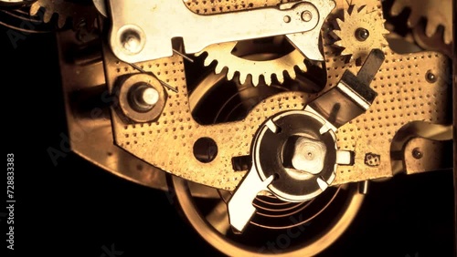 clockwork mechanism of an old ALARM CLOCK  disassembled with golden cogwheels running on silver steel closeup gear movement working front view detail swiss made antique watch isolated on black 4K HQ