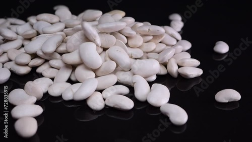 White beans cascading in slow motion onto a reflective black surface, poured from glass containers, perfect for vegan dishes. photo