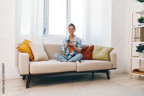 Smiling woman holding mobile phone on cozy sofa in living room © SHOTPRIME STUDIO