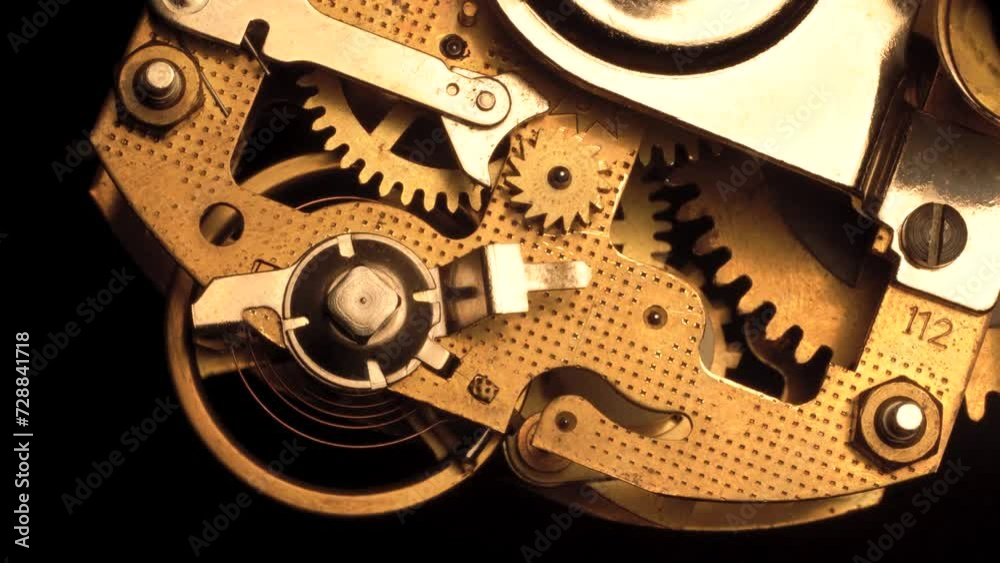 clockwork mechanism of an old ALARM CLOCK disassembled with golden cogwheels running slowly on silver steel closeup gear movement working close-up front view detail antique watch isolated on black