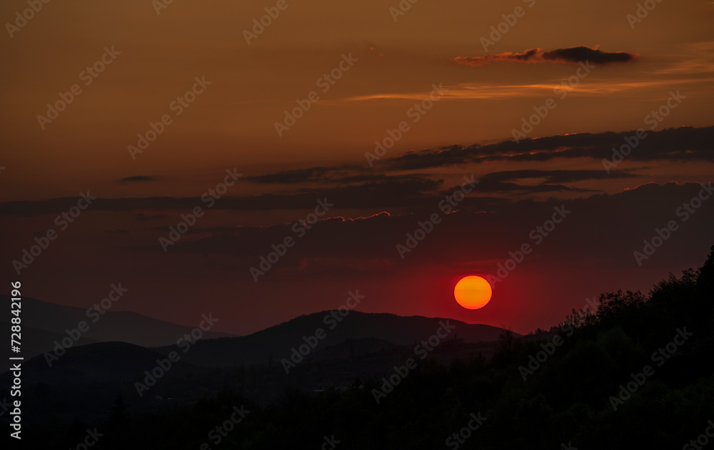 Fototapeta premium Beautiful sunset in the mountains. Sunset View from the Top of a Mountain. Sunset in strong orange tones in Serbia. The sun falls for horizon, a sunset. Shadows are condensed, beautiful clouds.