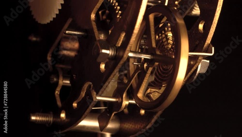 clockwork mechanism of an old ALARM CLOCK  disassembled with golden cogwheel running slowly on silver steel close-up gear movement working closeup low angle shot detail antique watch isolated on black