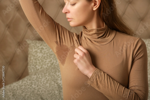  Close up image of woman in beige cotton turtleneck with sweat patch under armpit photo