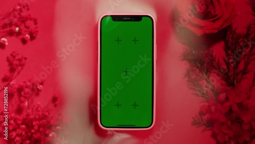 Phone with green screen chroma key on red and pink background with smoke close up , top view. Smartphone on summer bright texture studio shot. Composition of rose flowers and make photo