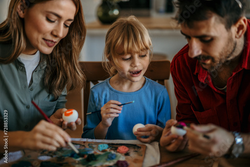 Parents and daughter share laughs while decorating Easter eggs