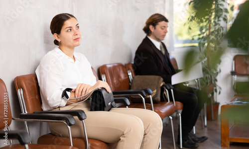 Young woman in business clothes is waiting on chair in office space