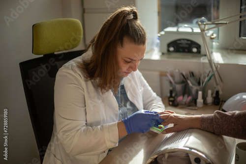 Female nail technician focused while doing her client's nail using electric nail file. 