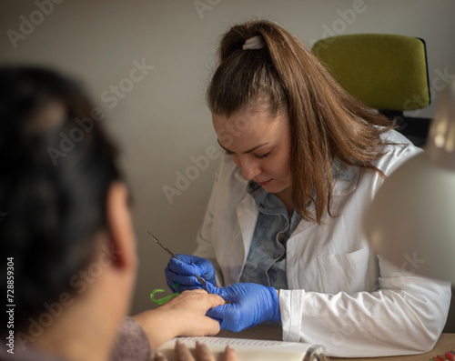 Female nail technician focused while doing her client's nail using electric nail file. 