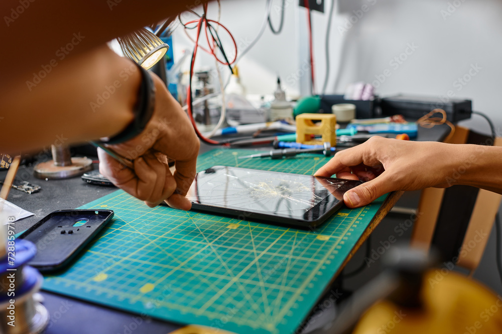 partial view of experienced technician removing broken touchscreen of digital tablet in workshop