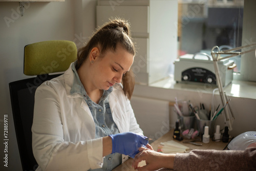 Female nail technician focused while doing her client's nail using electric nail file. 