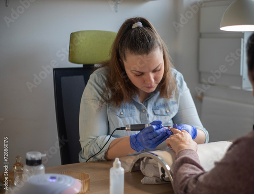 female caucasian Nail technician using electric nail file while working on clients nail