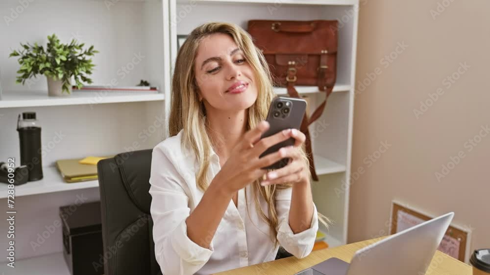 Bright young blonde woman worker, exuding confidence and positivity, enjoys successful business day. takes selfie picture with smartphone in elegant office interior, while working online on laptop.