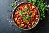Close up top view of a bowl of stewed cranberry beans in tomato sauce with herbs on a table