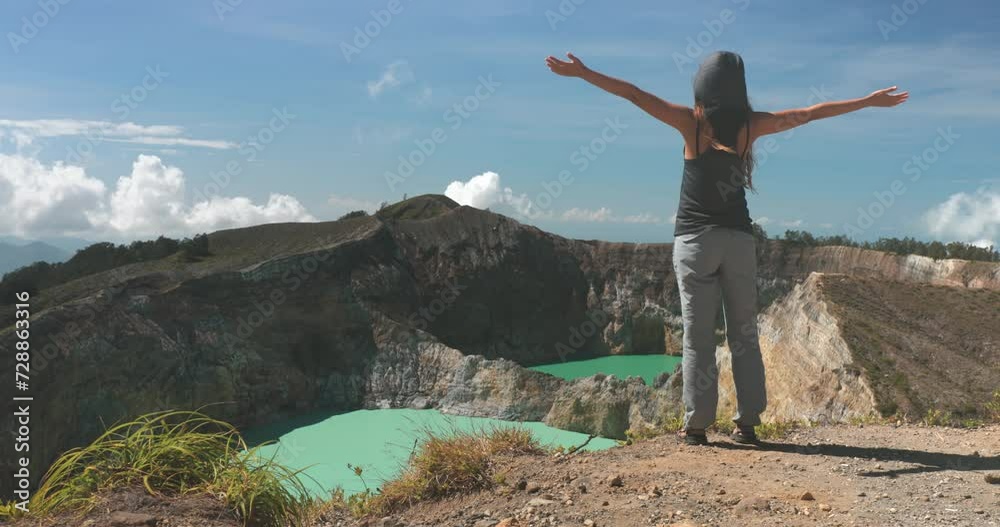 Woman raise hands on volcano mountain crater edge. Volcanic Kelimutu blue crater lakes. Travel destination. Beautiful wild landscape. Female tourist on summer vacation. Lifestyle holiday concept Woman raise hands on volcano mountain crater edge. Volcanic Kelimutu blue crater lakes. Travel destination. Beautiful wild landscape. Female tourist on summer vacation. Lifestyle holiday concept